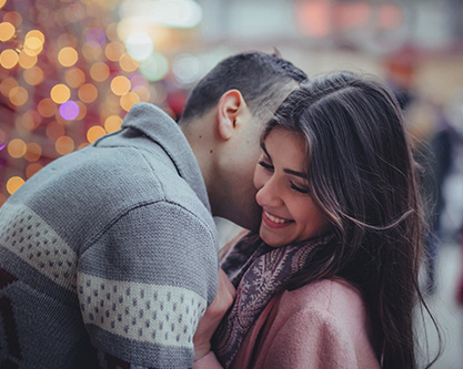 Dark haired couple embracing out front of The Hotel at Arundel Preserve