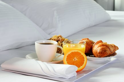 A tray of orange juice, granola, crescents & more on a bed at the Arundel Preserve Hotel